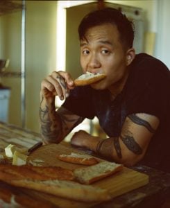Alessandro Jang, Founder of Out of Thin Air, eating a slice of bread with butter in a rustic kitchen setting.